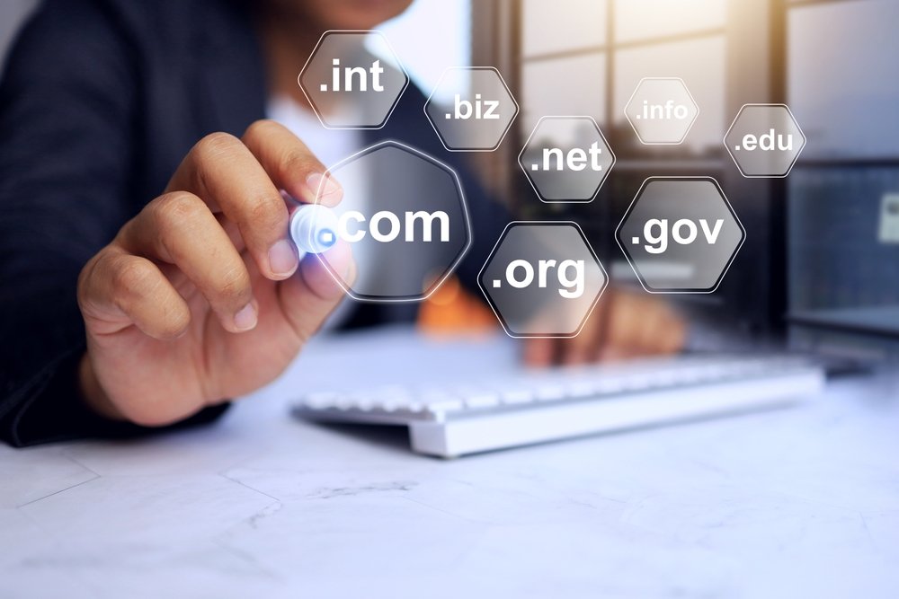 Businessman pointing to “.com” domain name extension on a digital interface showing various top-level domains like .org, .net, .gov, and .edu for website selection.