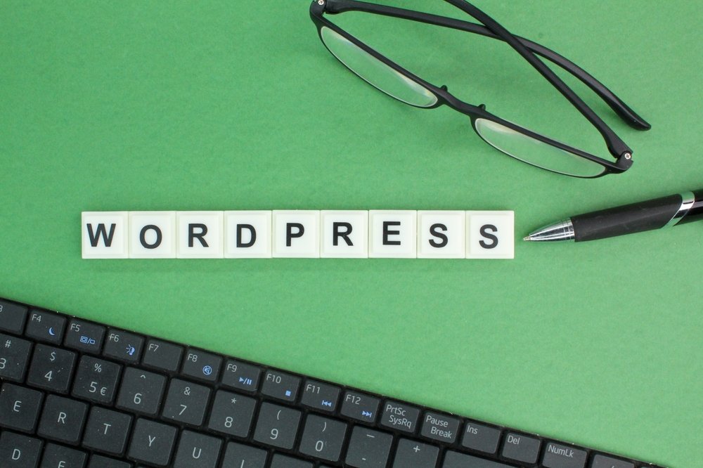 WordPress Website for Small Businesses and Startups concept featuring WordPress lettering on a desk with a keyboard, eyeglasses, and pen, representing website development and online business growth.